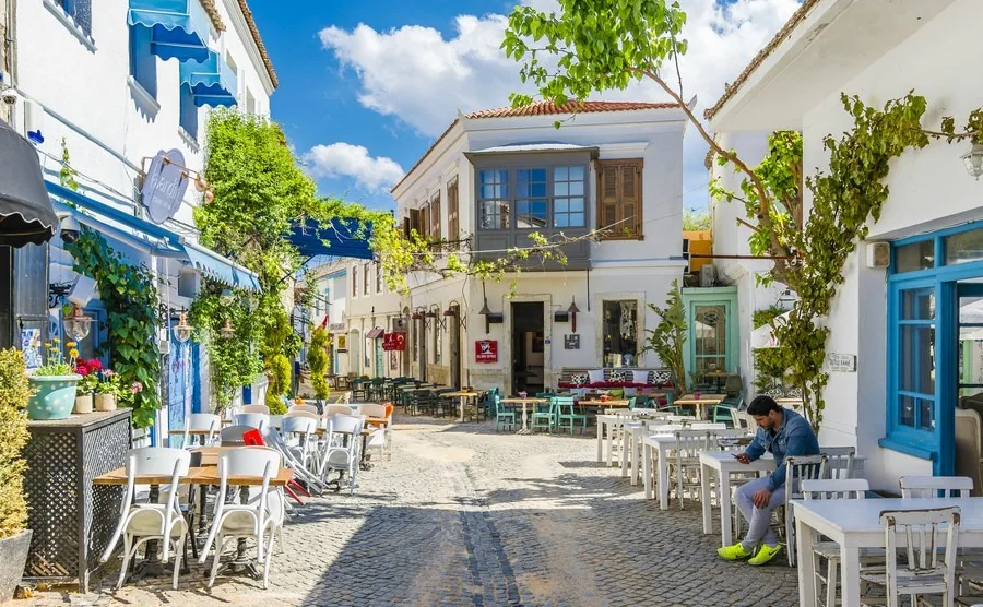 Cobblestone street in Alaçatı with white buildings, blue windows and outdoor café tables