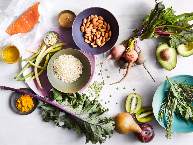 Salmon, avocado, beets, almonds, rice and assorted leafy greens arranged on a white surface.